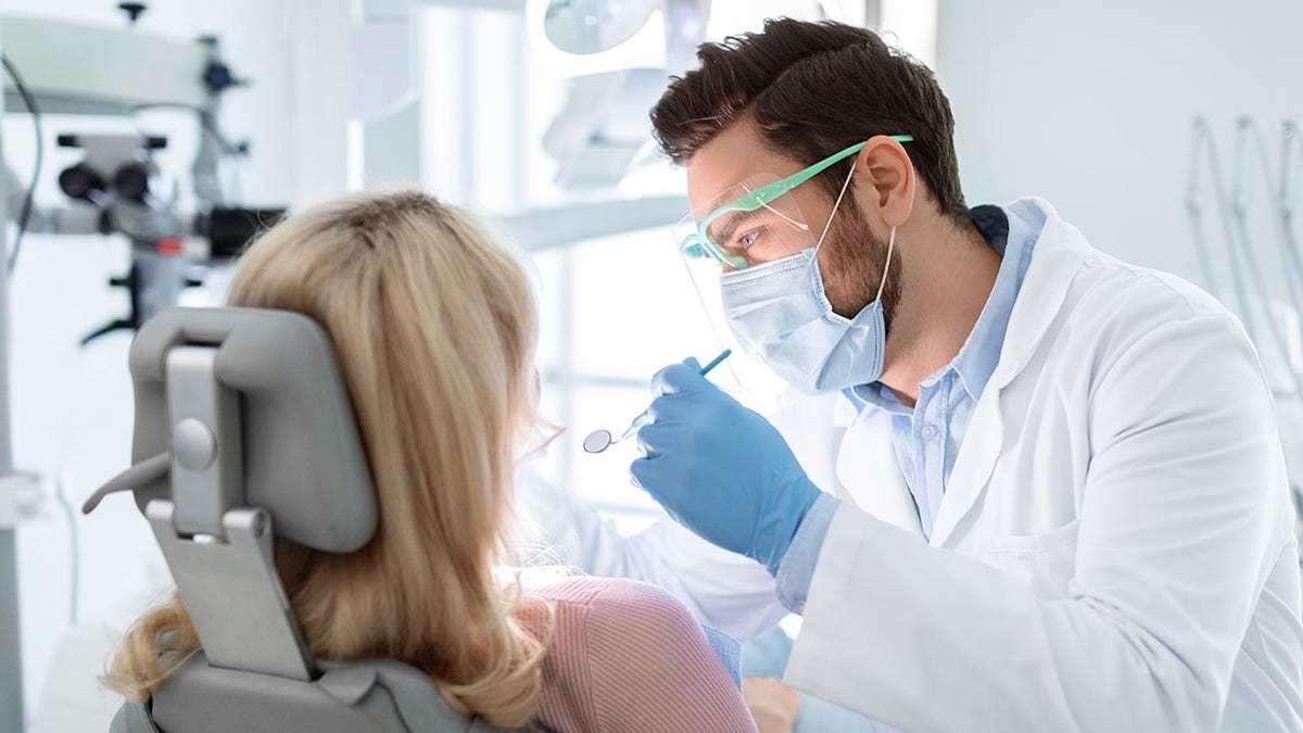 The dentist treats the woman in the dental chair.